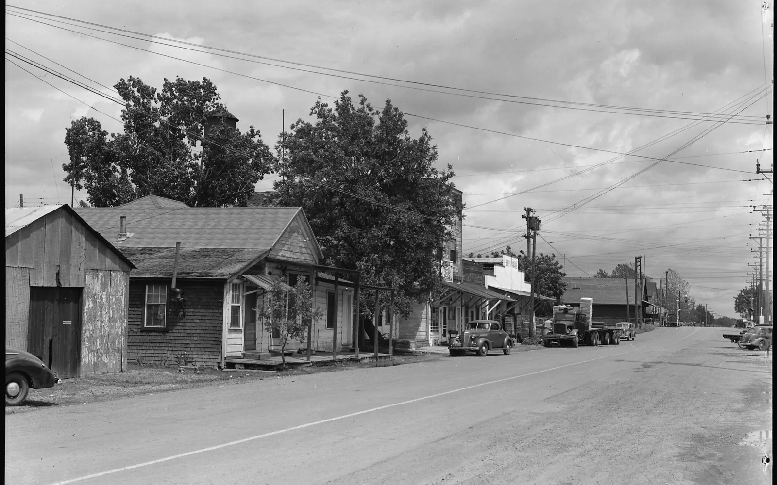 A black-and-white historical photograph of a main street in a small California agricultural town with storefronts and buildings along the street